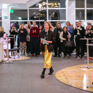 Festivaleröffnung im Foyer des Schauspiel Hannover. Das Foto zeigt Melanie Zimmermann. Sie geht durch das Foyer. Im Hintergrund applaudiert das Festivalpublikum.