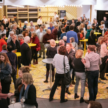 Das Foyer des Schauspiel Hannover während der Festivaleröffnung, mit zahlreichen Besucher*innen die sich an Stehtischen stehen und sich unterhalten.