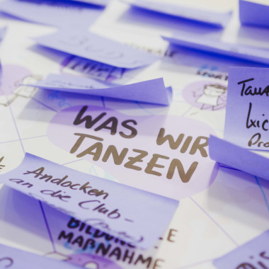 Mehrere Zettel in der Farbe lila, auf denen jeweils verschiedene Texte stehen. Darunter "Was wir tanzen"